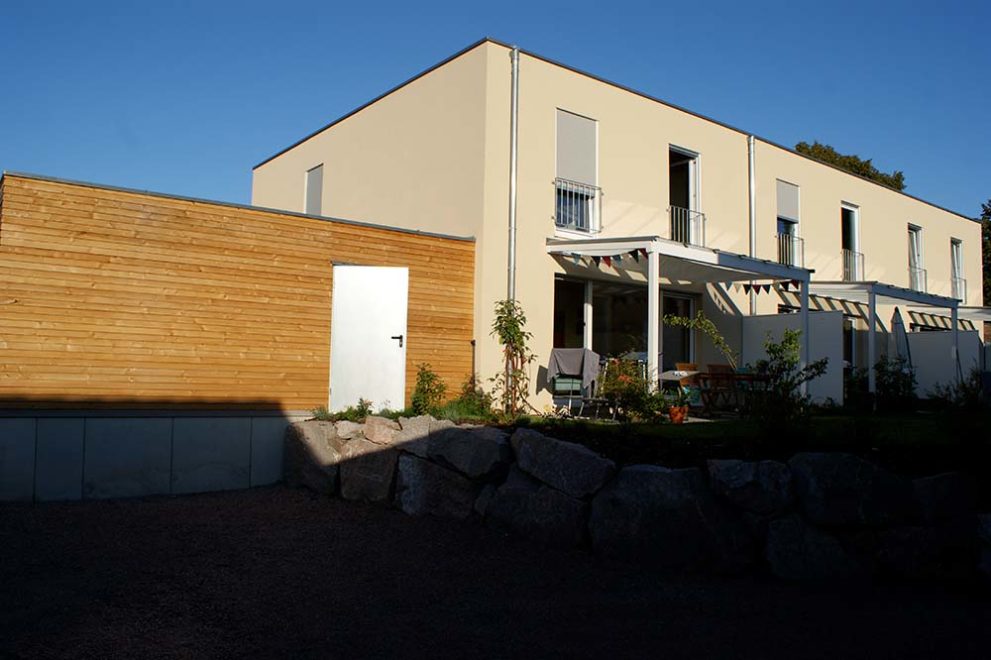 Terrasse eines Wohnhauses mit gelblicher Putzfassade, sowie eine Garage aus Holz nebendran.