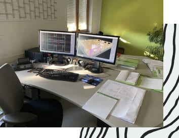 Schreibtisch mit zwei Bildschirmen vor einer grünen Wand