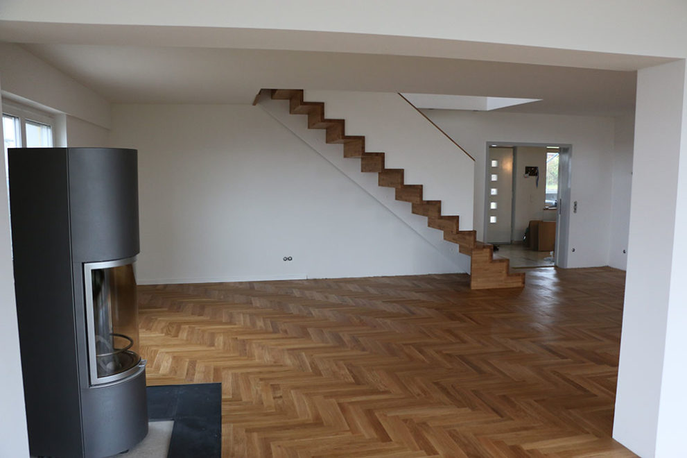 Wohnzimmer mit Holzboden und einem Holzofen, eine Holztreppe führt in den zweiten Stock