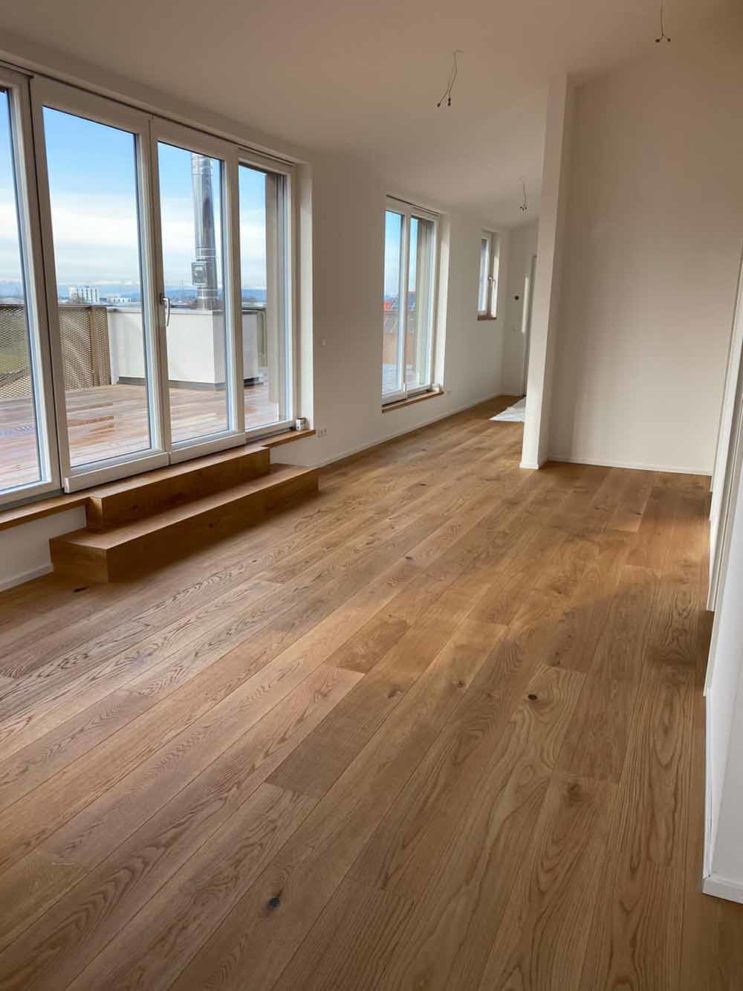 Zimmer mit Holzboden, große Fensterfront mit Ausgang zu Balkon