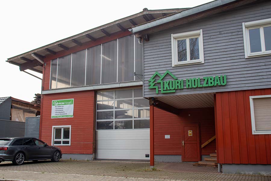 Gebäude in den Farben grau und rot mit der Aufschrift Kuri Holzbau in grün